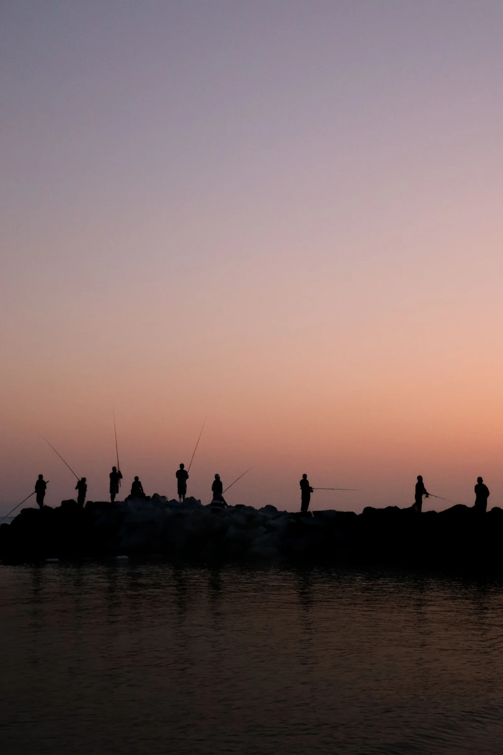 Silhouetted anglers casting from a rocky shore at sunset