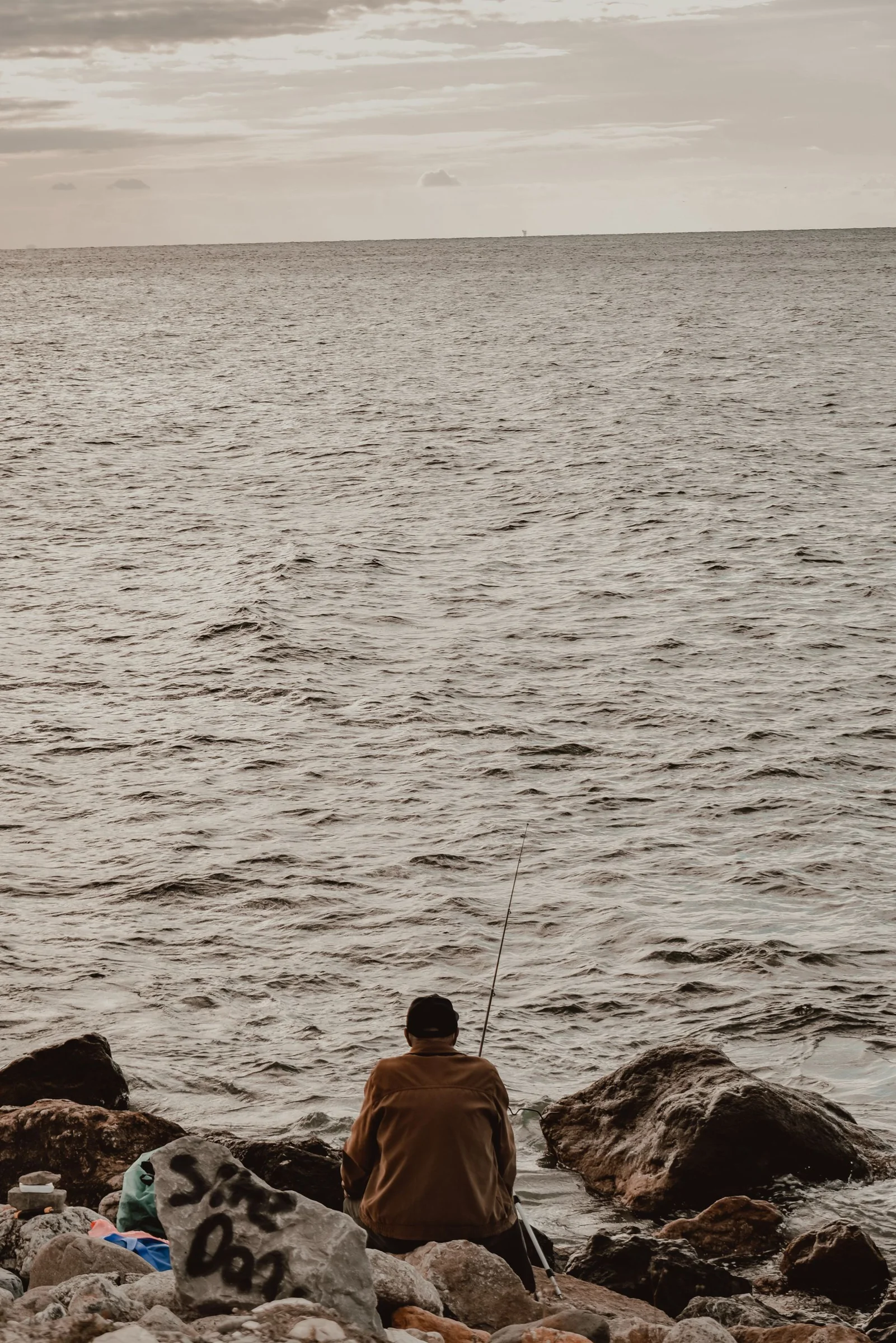 An angler seated on coastal rocks in evening light