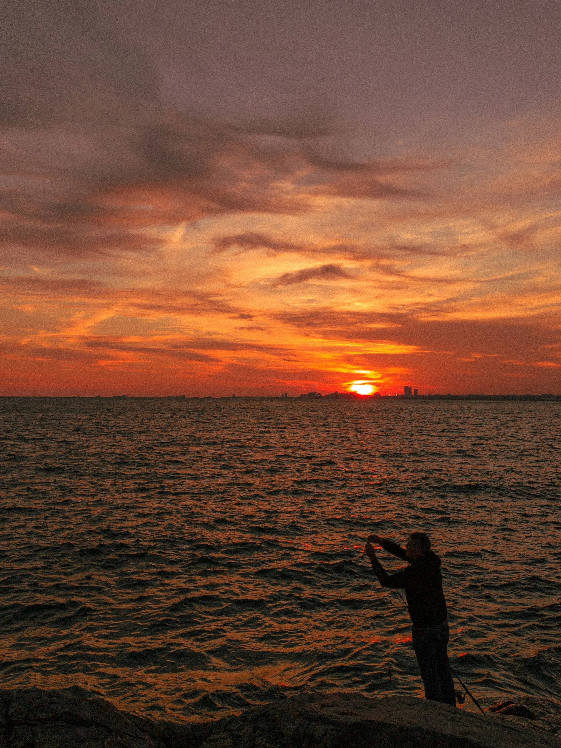 A fishing silhouette beneath a colourful coastal sunset
